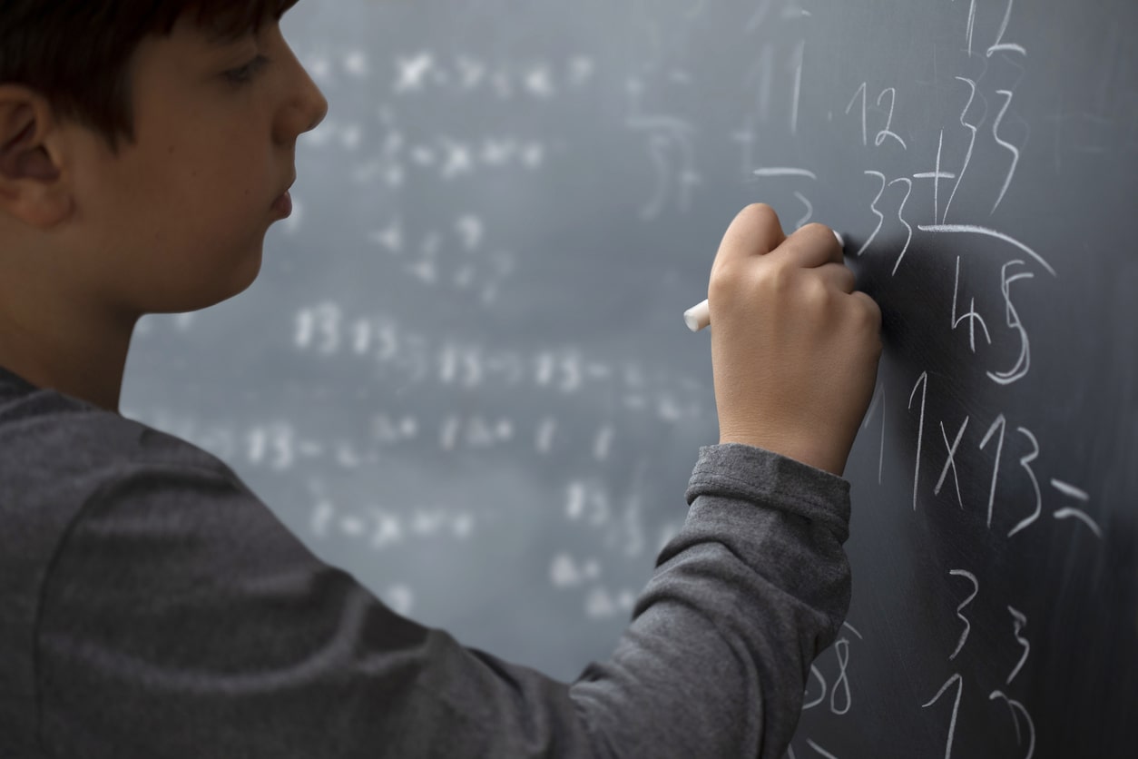 Student writes on the chalk board to solve a math problem using the make a table math strategy.